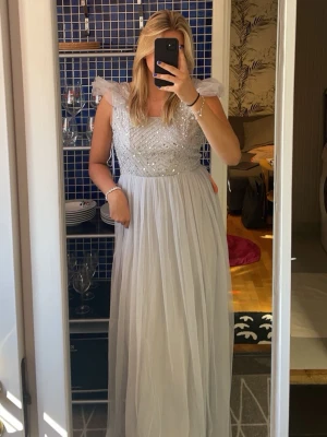 Balklänning med paljetter - En helt ny balklänning i ljusgrå/silvrig färg i storlek 40. Detaljerad med paljetter, tyllkjol och en dragkedja i ryggen. Originalförpackning och prislapp medföljer. Nypris: 1400kr. Väldigt bra kvalité.  Modell Tall, men passar såklart vanligtvis med, beroende på hur lång man vill ha den.  Referens: 178 cm lång och bär vanligtvis M/L och den sitter perfekt.