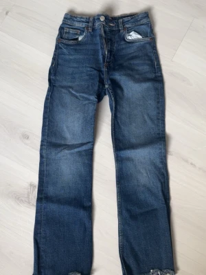 Blå raka jeans från Zara - Säljer ett par klassiska blå jeans från Zara med rak passform och fem fickor. Jeansen har en snygg tvättad look och råa kanter vid bensluten. Perfekta till en avslappnad stil och tillverkade i slitstarkt denimtyg.