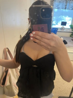 Svart ärmlös linnetopp med spets - Snygg svart linnetopp med smala axelband och v-ringad urringning. Toppen har spetsdetaljer och ett litet hål framtill under bysten för extra stil. Perfekt för dig som vill ha en luftig och trendig topp till sommaren.