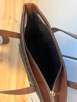 Brun och svart mönstrad handväska - Snygg handväska i brunt och svart med klassiskt rutmönster och långa axelband i brunt konstläder. Väskan har dragkedja upptill och rymligt huvudfack med svart innerfoder. Perfekt för dig som vill ha plats för allt du behöver under dagen. tyvär vet jag inte vart jag fick den ifrån då jag fick den för länge sen,pris går alltid att diskutera 