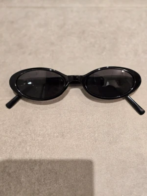 Svarta ovala solglasögon - Snygga svarta solglasögon med smal, oval form och blanka bågar. Klassisk och stilren look som passar till många outfits. Lätta att matcha och perfekta för soliga dagar.
