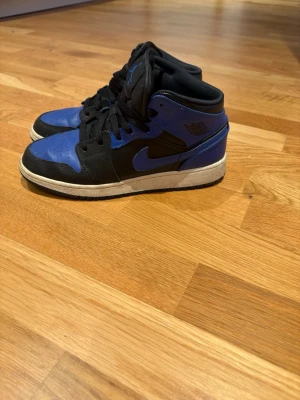 Nike Air Jordan 1 Mid svart/blå - Snygga Nike Air Jordan 1 Mid sneakers i färgen hyper royal, i storlek 38, i använt skick men fortfarande väldigt fina och välbehålda.