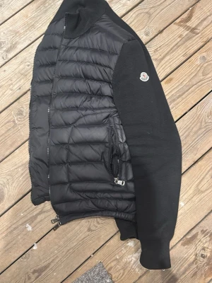 Svart pufferjacka från Moncler -  Söker mesta dels byten i samma pris klass. Snygg svart pufferjacka från Moncler med quiltad framsida och ärmar i mjukt tyg. Jackan har ribbade muddar, dragkedja framtill och två fickor med dragkedja. Moncler-logga på ärmen ger en exklusiv touch. Perfekt för kalla dagar.