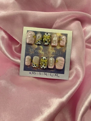 Bijou (XS);Short Ballerina - Snygga handgjorda press-on naglar i mix av ljusrosa, nude och vitt med prickar och guldfärgade dekorationer. Naglarna har en kort-ballerina form och coola 3D-detaljer som ger extra edge till din look. Perfekt för dig som vill sticka ut med trendiga naglar.