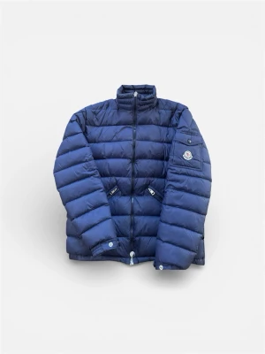 Blå dunjacka från Moncler - Snygg blå dunjacka från Moncler med hög krage och dragkedja framtill. Jackan har två fickor med dragkedja och en patch med Moncler-logga på ärmen. Strl 2, Bara att kontakta om du har några frågor🤩