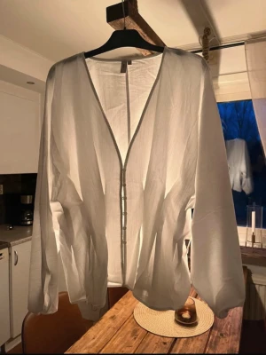 Vit blus med knappar från Nelly - Stilren vit blus från Nelly med v-ringning och knäppning framtill. Blusen har lång ärm och är tillverkad i ett tunt, lätt material som ger en luftig känsla. Perfekt att styla med jeans eller kjol för en trendig look. Aldrig använd och har prislappen kvar!💕