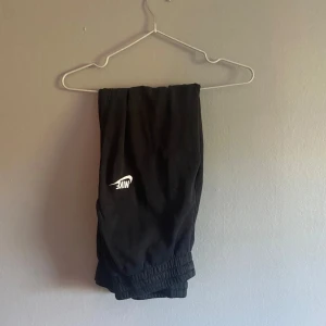 Svarta mjukisbyxor från Nike - Svarta mjukisbyxor från Nike med klassisk vit logga på benet. Byxorna har resår i midjan och vid bensluten för en skön och avslappnad passform. Perfekta för chill eller träning. Tillverkade i mjukt material som känns bekvämt hela dagen.