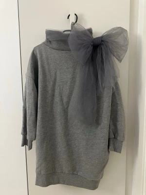 RED VALENTINO grå tröja, storlek S - Säljer en grå oversized hoodie med hög krage och en stor dekorativ rosett i tyll på axeln. Hoodien har långa ärmar med ribbade muddar och är gjord i mjukt sweatshirtmaterial. Perfekt för dig som vill sticka ut med en unik detalj!