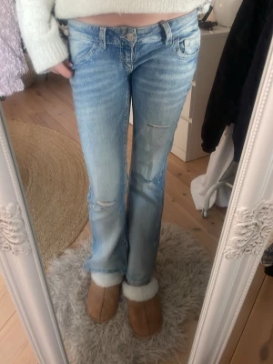 Ljusblå bootcut jeans med slitningar - Säljer ett par ljusblå bootcut jeans med slitna detaljer och snygga bakfickor. De är från Gina tricot 14+ i storlek S. Innerbana längd 77 cm och midja rakt över 38 cm. . Säljer då de är för korta. 