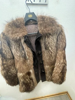 Brun pälsjacka med bred krage - Säljer en brun pälsjacka från Havgårds Malmö med bred krage och knappar framtill. Jackan har ett patchwork-mönster i olika bruna nyanser och är fodrad med quiltat tyg på insidan. Perfekt för dig som vill ha en statementjacka i vinter.