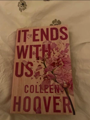 It Ends With Us av Colleen Hoover - En gripande roman av Colleen Hoover med omslag i träfärgad ton och rosa blommor. Boken handlar om kärlek, svåra val och relationer. Perfekt för dig som gillar känslosamma berättelser och starka karaktärer. Pocketutgåva på engelska.