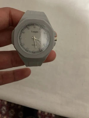 Grå klocka från Timetti - Stilren grå klocka från Timetti med rund urtavla och tydliga markeringar. Klockan har ett sportigt formspråk och ett armband i syntetmaterial. Perfekt accessoar för dig som gillar enkel och modern design.