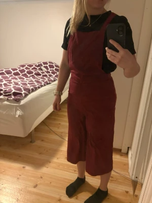 H&M vinröd jumpsuit i storlek 36 - Säljer en vinröd jumpsuit med croppade, vida ben och breda axelband som korsas i ryggen. Jumpsuiten har hög midja och är gjord i ett mjukt tyg, perfekt för en avslappnad men ändå snygg look. Inget synligt märke på plagget.