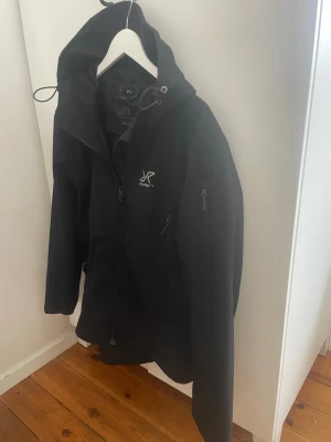 Svart vindjacka från RVRC - Snygg svart vindjacka från RVRC  med huva och dragkedja framtill. Jackan har två sidofickor med dragkedja och en bröstficka. Tillverkad i ett slitstarkt material som står emot vind. Perfekt för blåsiga dagar och outdoor-aktiviteter. Sorlen S men passar M. Använd 2 gånger.