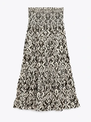 Svartvit mönstrad långkjol från zara - Säljer en svartvit långkjol med ett unikt grafiskt mönster. Kjolen har smock i midjan för skön passform och volangdetaljer som ger extra rörelse. Perfekt för dig som gillar statement-plagg och vill sticka ut lite extra.