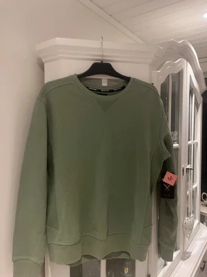 Grön sweatshirt från Denim Day - Snygg grön sweatshirt från Denim Day med rund halsringning och ribbade muddar vid ärmslut och nederkant samt ribbade detaljer på sidan. Tröjan har en klassisk relaxed fit och är tillverkad i mjukt material som passar perfekt till vardagslooken.