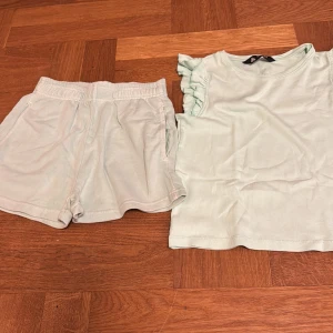 Sommarset - Säljer en söt ljusgrön topp med volangdetaljer på ärmarna. Perfekt för varma dagar och ger en fräsch look. Toppen är i ett mjukt material som känns skönt mot huden. Shortsen har en liten fläck längst ner som är en skvätt av hallon! Går säkert att få bort!