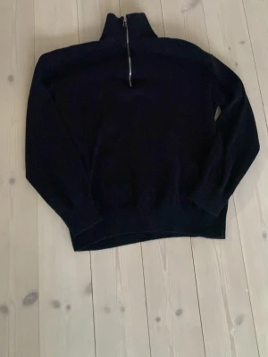 Svart halvzip tröja med hög krage - Mysig svart tröja med halv dragkedja och hög krage. Tröjan har långa ärmar och ribbade muddar. Perfekt för lager på lager och enkel att matcha med olika outfits. Liten defekt då dragkedjan är böjd 