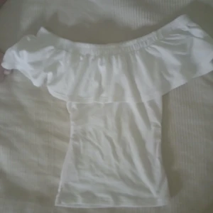 Vit offshoulder topp med volang - Säljer en söt vit offshoulder topp med volang rund axlarna från gina tricot i storlek xs. Jag har sytt in den vid midjan så den ska få en tightare passform, tyget är väldigt stretchigt.  Det syns lite rosa streck i sidorna där jag sytt om den men de är inget man tänker på när man har på sig den!💕