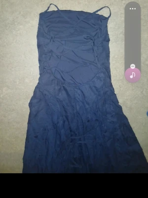 Marinblå långklänning med snörning - Säljer en marinblå långklänning med tunna axelband och snygga snörningsdetaljer framtill. Klänningen har en utställd kjol och är perfekt för dig som vill ha en elegant och enkel look. Materialet känns lätt och flowy.