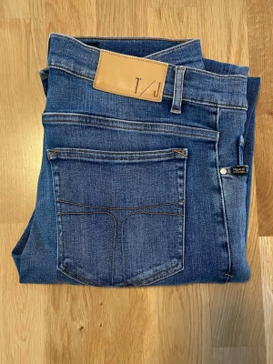 Blå skinny jeans från Tiger of Sweden - Säljer ett par klassiska blå skinny jeans från Tiger of Sweden. Jeansen har en snygg mellanblå tvätt, fem fickor och läderpatch med logga bak i midjan. Perfekta till en avslappnad stil och sitter tight hela vägen ner. Fråga om mått!