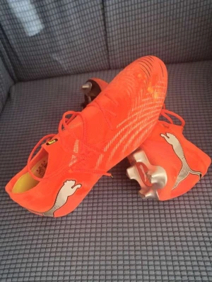 Puma Future Orange Fotbollsskor Elite  - Säljer ett par grymma orangea Puma Future fotbollsskor med vita detaljer och silvriga dobbar. Skorna har snörning, låg profil och är tillverkade i syntetmaterial för bästa känsla på planen. Perfekta för dig som vill sticka ut och ha bra grepp på konstgräs eller gräs.