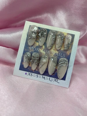 SilverMuse (XS);Medium Almond - Snygga handgjorda press-on naglar i beige med handmålade silverfärgade 3D-metall dekorationer och abstrakta mönster. Naglarna har en medium, almond form och ger en edgy look. Perfekta för dig som vill sticka ut med unika detaljer. Kommer i XS: 14 mm, 11 mm, 11,5 mm, 10 mm, 8 mm.