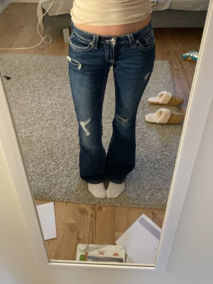 Blå bootcut jeans från Gina Tricot - Snygga mörkblå jeans från Gina Tricot i bootcut-modell med låg midja. Jeansen har slitna detaljer, kontrastsömmar och broderad bakficka. Säljer då jag har två och dessa inte satt lika bra som de andra!💗