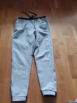 Grå mjukisbyxor från Under Armour - Snygga grå mjukisbyxor från Under Armour med resår i midjan och justerbar dragsko. Byxorna har muddar vid bensluten och en diskret logga på benet. Perfekta för chill eller träning, tillverkade i ett mjukt och lätt material.