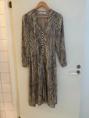 Adoore klänning - Snygg långklänning från adoore med zebramönster i beige och svart. Klänningen har v-ringning, knappar framtill och långa ärmar. Säljer då jag inte tyckte den passade just mig ( priset går att diskutera med snabb affär) 