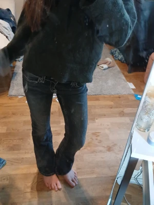 Svarta bootcut jeans - Säljer ett par svarta bootcut jeans med vita kontrastsömmar och klassiska fickor. Jeansen har låg midja och silverfärgad knappdetalj. Perfekta för en avslappnad och trendig look.