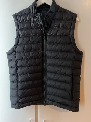 J.lindeberg väst - Snygg svart dunväst från J.lindeberg med quiltad design och hög krage. Västen har dragkedja framtill och två sidofickor med dragkedja. Perfekt för lager-på-lager och håller dig varm under kyliga dagar. Bra skick, Storlek M men passar S också