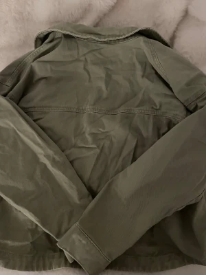 Olivgrön jeansjacka från Vero Moda - Snygg olivgrön jeansjacka från Vero Moda. Klassisk modell med krage och raka sömmar. Perfekt att slänga över en hoodie eller t-shirt för en avslappnad look. Tillverkad i slitstarkt denimtyg.