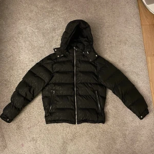 Bandit Europe Jacket - Säljer en svart pufferjacka med huva och dragkedja framtill. Jackan är oanvänd. Nypris 2200 kr. Sitter true to size