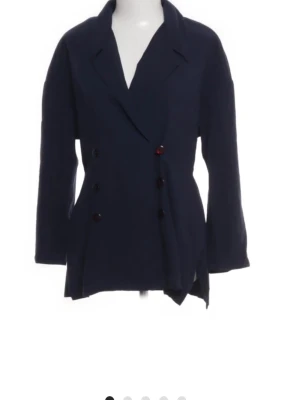 Mörkblå dubbelknäppt kavaj - Stilren mörkblå kavaj med dubbelknäppning och klassisk krage. Kavajen har långa ärmar och en något lös passform. Perfekt för dig som vill ha en tidlös och enkel look. Materialet ser ut att vara lätt och bekvämt, vilket gör den enkel att bära till olika outfits.