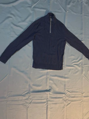 Mörkblå stickad tröja Jack & Jones - Snygg mörkblå stickad tröja från Jack & Jones Premium med halv dragkedja vid halsen. Tröjan har lång ärm och ribbade muddar vid ärmslut och nederkant. Perfekt för lager på lager och enkel att matcha med jeans eller chinos.