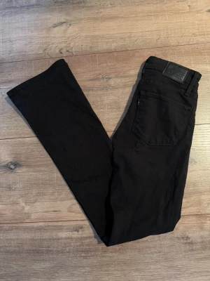 Levi’s Svarta Bootcut 725  - Säljer ett par svarta jeans från Levi's med klassisk femficksmodell och rak passform. Jeansen har en svart läderpatch bak i midjan och är tillverkade i ett mjukt bomullsmaterial med lite stretch. Perfekta för en clean och stilren look.
