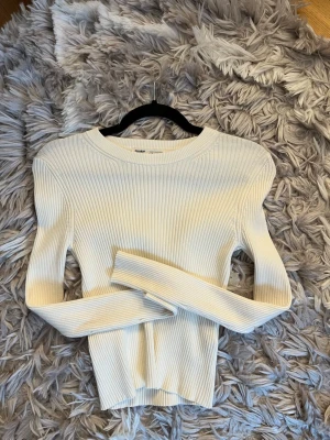 Vit ribbstickad tröja Pull&Bear - Säljer en vit ribbstickad tröja från Pull&Bear med lång ärm och rund halsringning. Tröjan har en tight passform och är gjord i ett mjukt, stretchigt material som sitter snyggt på kroppen. Perfekt att styla med jeans eller kjol. Skulle säga att den passar en Xs mer än en M 
