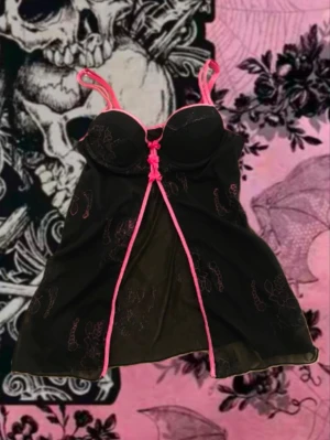 Svart babydoll från native intimates  - Söt svart tröja med vadderade kupor, rosa spetsdetaljer och små rosetter framtill, det är även rosa blomdetaljer. Tunnt material och justerbara axelband i rosa. Tröjan kan även användas till nattlinne!