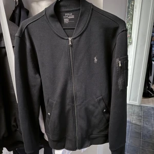 Ralph lauren zip up - Säljer nu denna jättefina svarta ralph lauren zip up. Funkar perfekt som vårjacka/höstjacka. Den är fint skick trots en del användning och den är i strl M. Bara att skriva ety DM vid intresse!