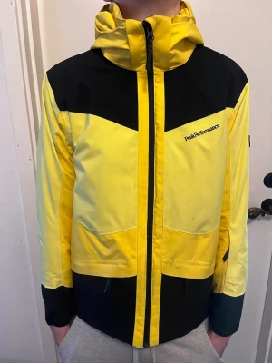 Gul och svart vindjacka Peak Performance - Snygg gul och svart vindjacka från Peak Performance med huva och dragkedja framtill. Jackan har sportig design med kontrastpaneler, hög krage och logga på bröstet. Perfekt för blåsiga dagar och outdoor-aktiviteter. Skicket är 8/10 pga lite smutsig men annars fint skick. 