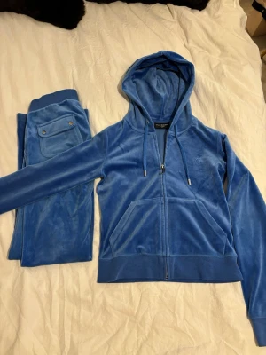 Blåa mjukisbyxor från Juicy Couture - Säljer ett par blåa mjukisbyxor från Juicy Couture. Byxorna har bakficka med knapp och matchar perfekt med hoodie i samma färg. Sliver detaljer. Skön passform. Byxor-XXS men funkar som XS också. Tröja-XS. 