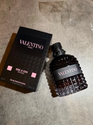 Valentino Uomo Born In Roma Intense EdP - Valentino Uomo Born In Roma Intense Eau de Parfum i 100 ml. Flaskan har en mörk, nästan svart färg med diamantmönstrad yta och svart kork. Förpackningen är svart med rosa detaljer och tydlig Valentino-logga. En lyxig och modern herrdoft. Kvitto finns 