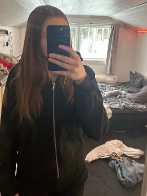 Zipphoodie - Säljer en svart hoodie med dragkedja framtill och huva. Hoodien har en enkel och stilren design, perfekt för en avslappnad look. Materialet känns mjukt och bekvämt, och den har ribbade muddar vid ärmslut och nederkant.