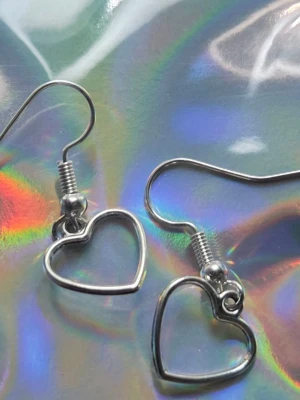 Silvriga hjärtformade örhängen Rostfritt Stål Nya - Söta örhängen med två sammanflätade hjärtan på varje krok.  ✔️ Material: Rostfritt stål ✔️ Färg: Silver ✔️ Skick: Nya / oanvända / Handgjorda av mig  ✔️ Lätta & bekväma att bära Perfekta som present eller till vardag/fest. Frakt: Samfraktar gärna.