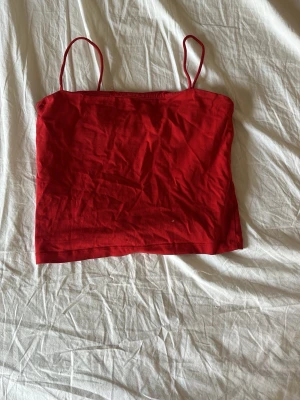 Röd ärmlös linnetopp - Snygg röd linnetopp med tunna axelband och rak skärning. Perfekt till jeans eller kjol för en enkel och trendig look. Tillverkad i mjuk bomull som känns skön mot huden.