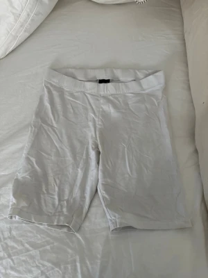 Vita cykelshorts i bomull - Säljer ett par vita cykelshorts med elastisk midja. De är enkla och stilrena, perfekta till sommaren. Materialet känns mjukt och stretchigt, vilket gör dem bekväma att bära hela dagen.