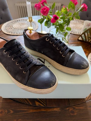 Navy blue sneakers från Lanvin - Stilrena navy blue sneakers från Lanvin med ovandel i mocka och tåparti i slätt läder. Skorna har blåa skosnören, metallfärgade öljetter och en vit sula som ger en snygg kontrast. Perfekta för dig som gillar klassisk men trendig stil.