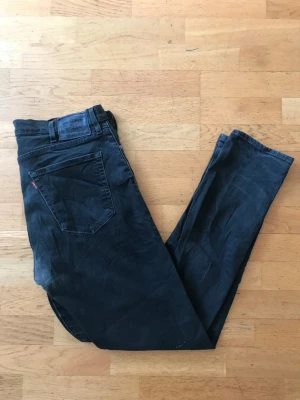 Svarta Levi's 512 jeans med rak passform - Säljer ett par svarta jeans från Levi's med klassisk rak passform och fem fickor. Jeansen har en diskret tvättad look, bälteshällor och Levi's ikoniska röda etikett på bakfickan. Perfekta för en avslappnad och stilren outfit.