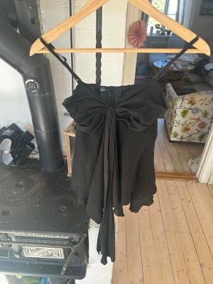 Svart linnetopp med rosett - Snygg svart linnetopp med tunna axelband och stor rosettdetalj framtill. Toppen har en flowy passform och är perfekt för att lyfta vilken outfit som helst. Materialet känns mjukt och lätt, vilket gör den skön att bära under varma dagar.